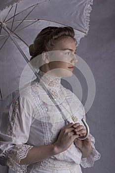 Edwardian woman in white blouse and skirt standing against a studio backdrop