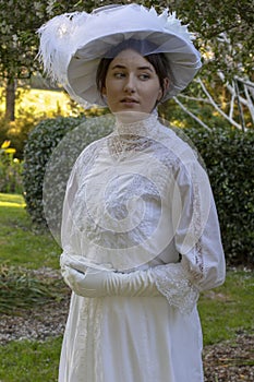 Edwardian woman in white lace outfit and large hat in a garden
