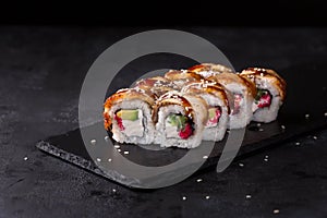 Eel sushi rolls on a stone plate over black background