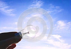 Eelectrical light bulb in hand on blue sky background. Hand holding light bulb on a background sky and sun.