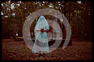 The eerie photo captures a ghost holding a jack\'s pumpkin while standing in a graveyard at dusk. Halloween