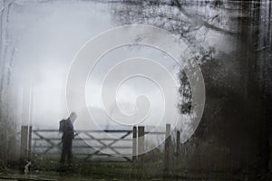 An eerie silhouette of a lone hooded figure with a rucksack by a gate surrounded by trees. With a dark, spooky blurred abstract, g