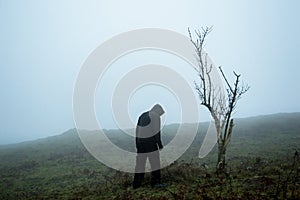 An eerie spooky figure standing by a tree on a foggy winters hillside