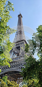 Effel tower in Paris against a bright blue sky and green trees