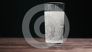 Effervescent pill dissolving into a glass of water, slow motion.