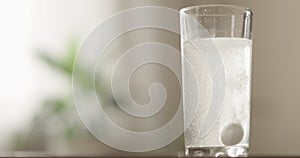 Effervescent tablet dissolving with fizz in a water glass indoors with a green plant and window on the background a concept of hea