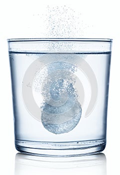 Effervescent tablet dissolving in a glass of water. Isolated on white background photo