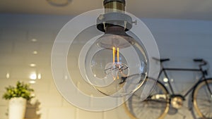 Efficient incandescent light bulb waste electricity against a tiled wall with a small bike and a plant pot.