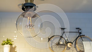 Efficient incandescent light bulb waste electricity against a tiled wall with a small bike and a plant pot.