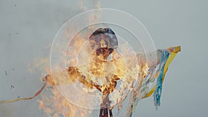 An effigy of Maslenitsa burns in a strong fire against a cloudy blue sky. The pagan feast of the Maslenitsa and the
