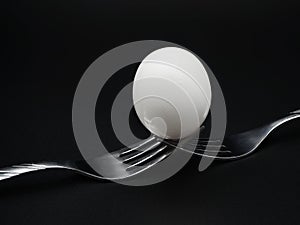 Egg balanced on two forks isolated on black background.