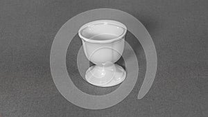 Egg cup, white, ceramic, against a solid grey cloth background