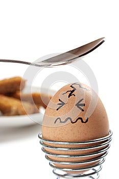Egg with drawn face, about to be hit with teaspoon