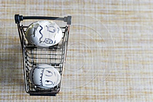 An egg with a drawn medical mask looks scared at a cracked egg in metal mini cart.