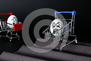 Egg with drawn scared face in shopping cart stunting on background photo