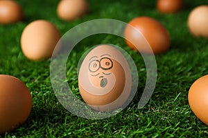 Egg with drawn surprised face among others on green grass