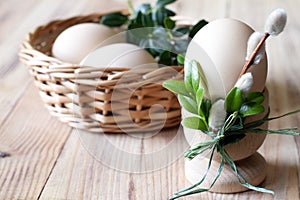 Egg in egg cup decorated catkins and boxwood and eggs in basket on wooden background, easter concept