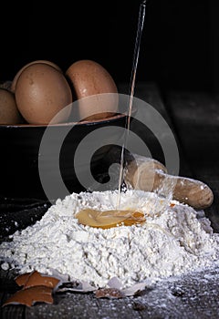 Egg falling on flour, bottom bowl with eggs and wooden kneader