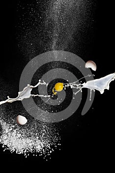 Egg in flight, milk and flour on black background. Scattering egg shels