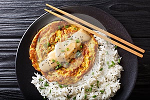 Egg foo yong fried egg patty containing vegetables  and meat with rice garnish close-up on a plate. horizontal top view