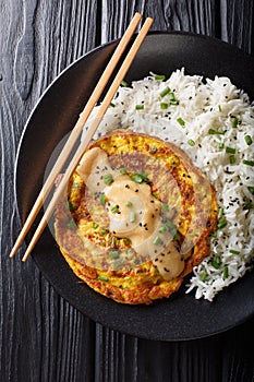 Egg foo yong fried egg patty containing vegetables  and meat with rice garnish close-up on a plate. Vertical top view