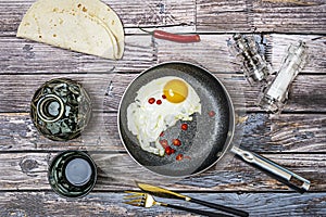 Egg fried in olive oil with slices of red hot chili peppers inside a frying pan with glass and bottle of liquor, photo