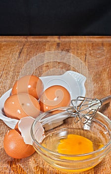 Egg in glass bowel with whisk, egg shells and three brown eggs