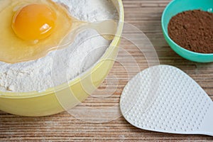 Egg hammered in a bowl of flour, next to a bowl of cocoa