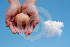 Egg in hands on blue sky background with cloud