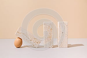 Egg holding a travertine marble block on a beige and gray background. 2021 Easter unique still life concept.