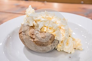 Egg Mayonnaise filling on a baked jacket potatoe on white plate with cutlery on a wooden table in a cafe