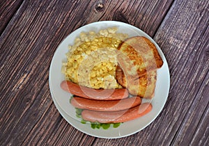 Egg omelet, bread croutons and boiled sausages on a wooden table