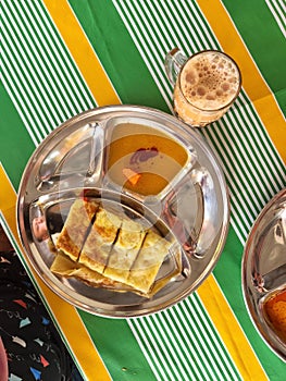Egg paratha or Roti telur with gravy in a metal plate with teh tarik or milk tea.