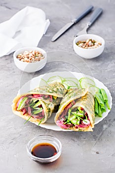 Egg rolls filled with pastrami, vegetables and green onions on a plate, sprouted grains and soy sauce in bowls on the table.