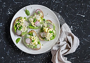 Egg scrambled sandwich's with green peas and radishes on a dark stone background.