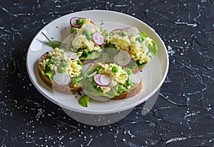 Egg scrambled sandwich's with green peas and radishes on a dark stone background.