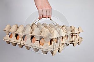 Egg tray with brown chicken eggs on gray background. Person carries a full carton package of eggs
