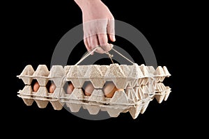 Egg tray isolated on black background. Brown chicken eggs in cardboard package in hand