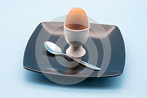 egg in a white cup with a spoon on a black plate isolated against a blue background