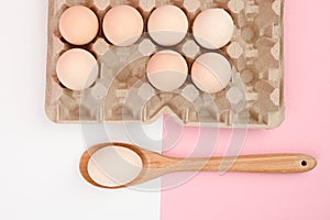 Egg on a wooden spoon. A tray of eggs on a white and pink background. eco tray with testicles. minimalistic trend, top view. Egg