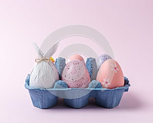 Egg wrapped in a paper in the shape of a bunny with colorful Easter eggs in carton tray. Minimal Easter concept