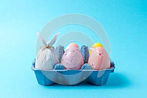 Egg wrapped in a paper in the shape of a bunny with colorful Easter eggs in carton tray. Minimal Easter concept