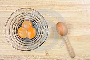 Egg yolk in glass bowl and raw egg in wood spoon