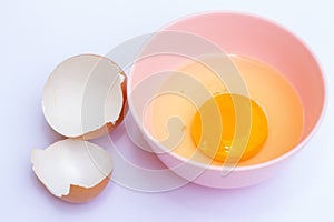 Egg yolk in a pink bowl with an eggshell on the white background