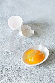 Egg yolk in a white bowl with a shell on a gray background. Egg.