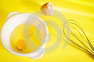 Egg yolks with a whisk on a yellow background