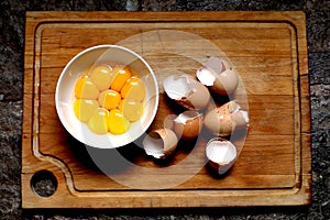 Egg yolks in a white bowl and egg shells on a wooden background