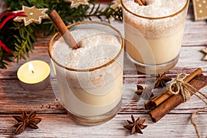 Eggnog in glass cups with a delicate foam, spices and a cinnamon stick