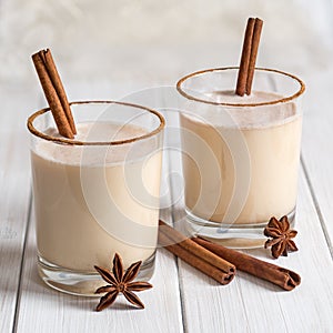 Eggnog in glass cups with a delicate foam, spices and a cinnamon stick