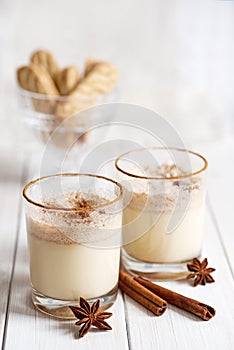 Eggnog in glass cups with a delicate foam, spices and a cinnamon stick